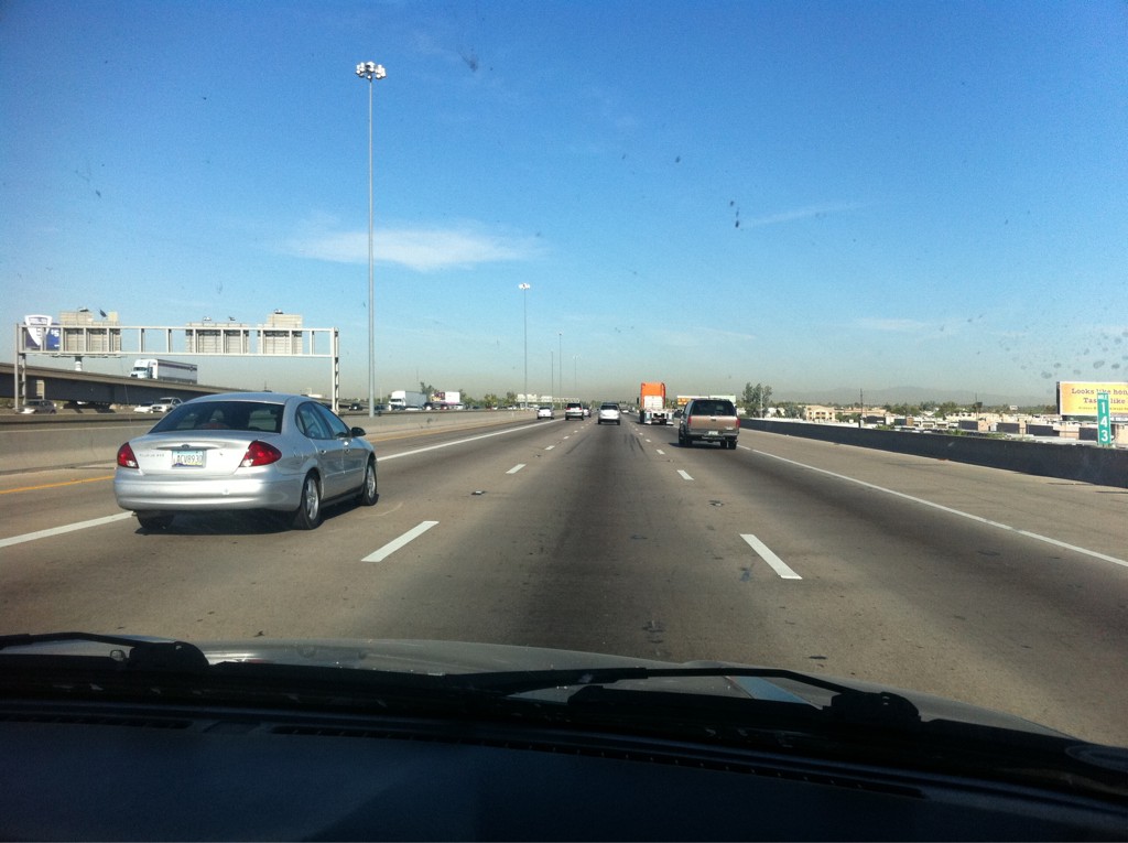 Photograph out the windsheild of a car driving on the freeway. Mountains appear on the horizon.