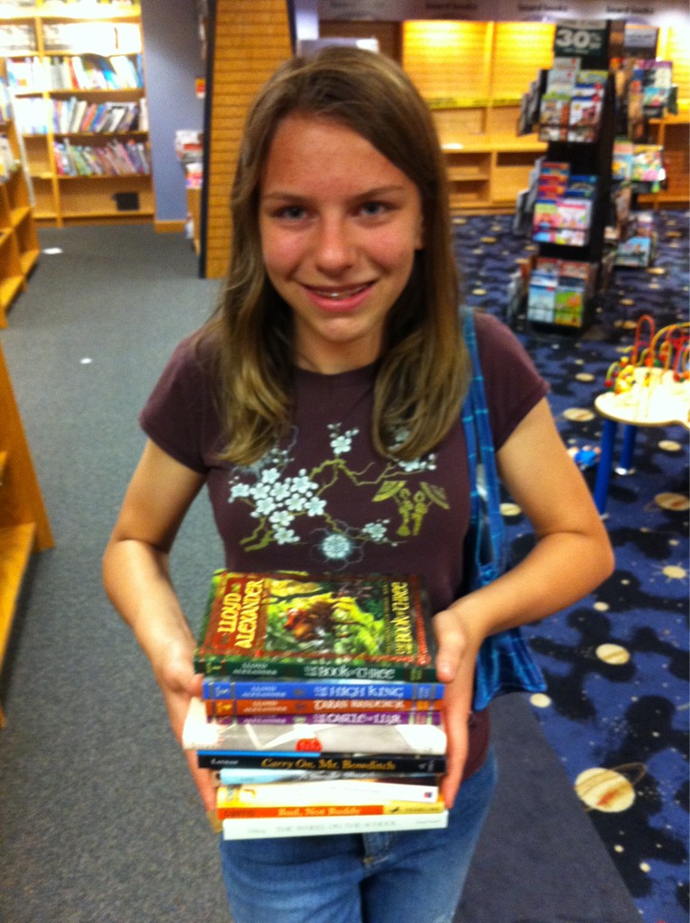 A teenager posing for the camera in a someone-decimated-looking Borders book store. They hold a large pile of books.