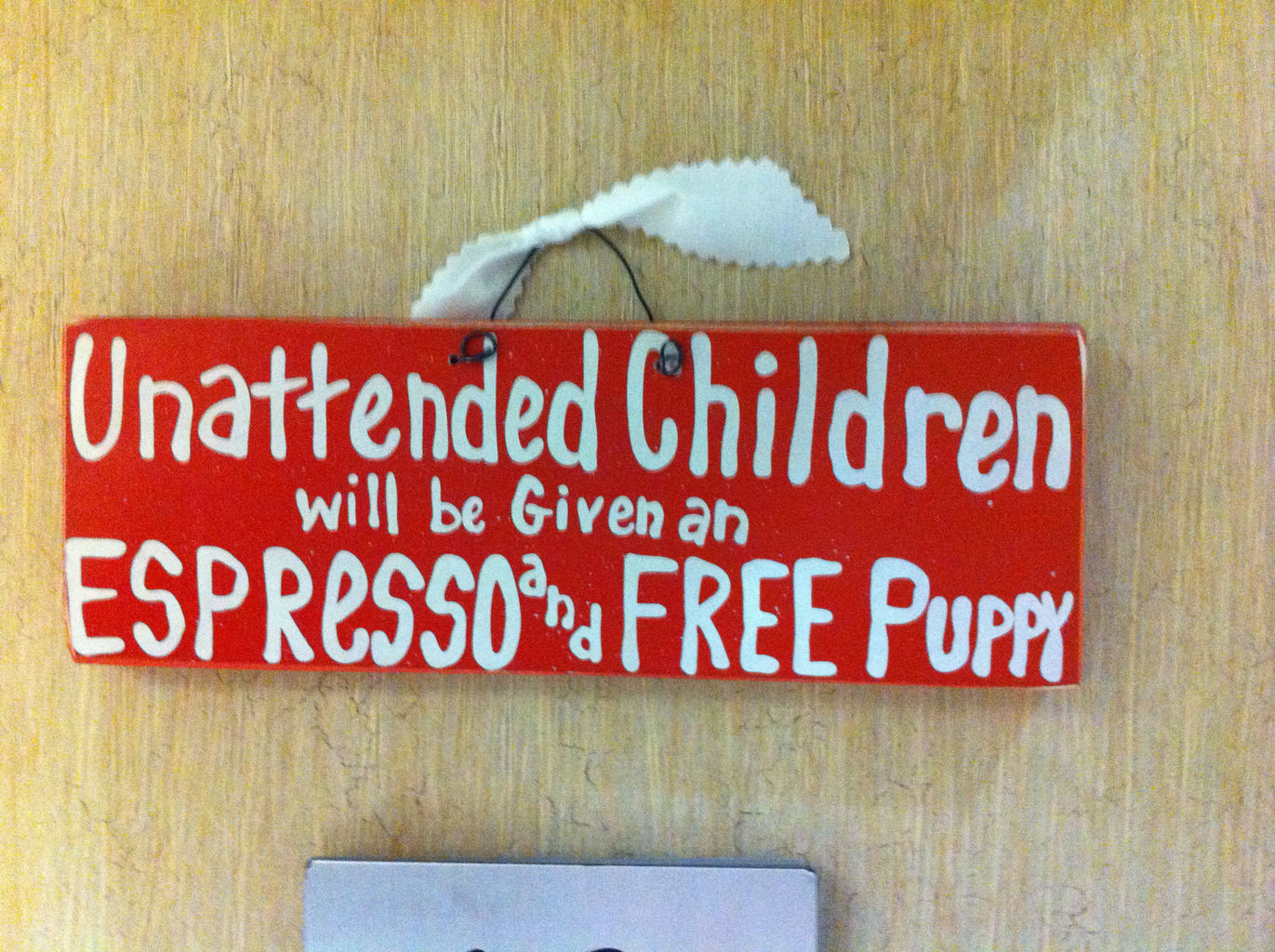 A decorative hand-painted wooden sign that reads "Unattended children will be given an espresso and a free puppy".