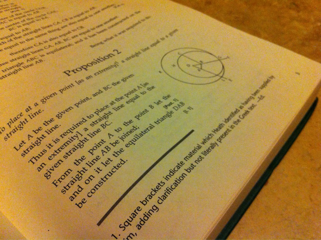 A geometry textbook open to a page describing Euclid's Proposition 2. The book layes open on a table and the photo frames only a portion of the right-side page.