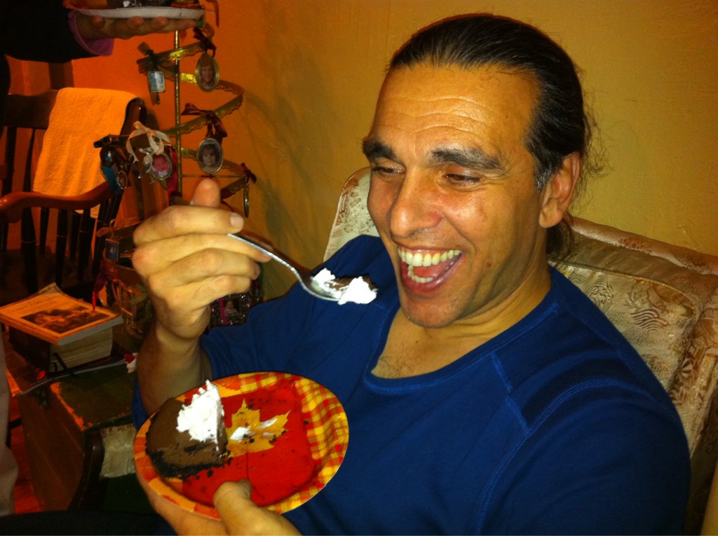 A middle aged man with long pulled back hair smiles as he's about to take a bite of chocolate pie with whipped cream.