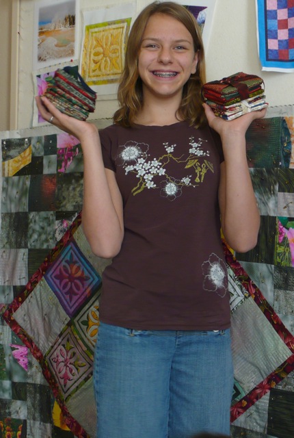 A teenager smiles for the camera. They hold a stack of cloth drink coasters in each hand.