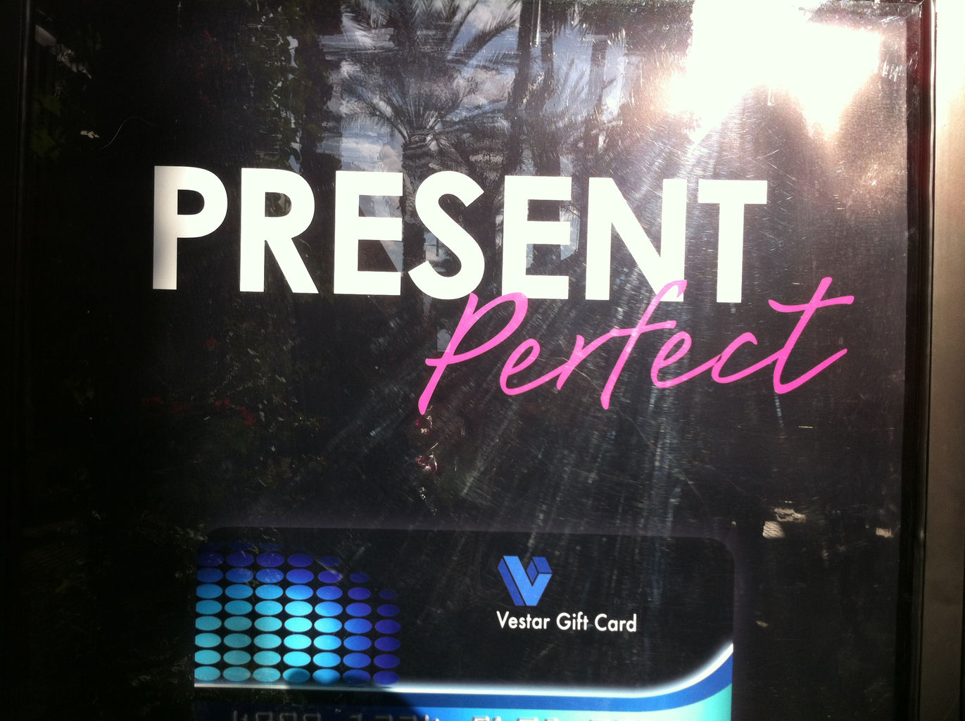 A sign board at a mall showing a large print add. In tall letters it says "Present Perfect". Below it shows a gift card.