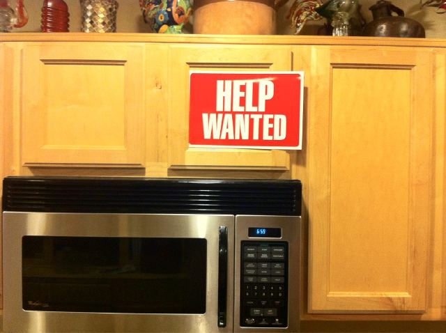 A close crop of kitchen cabinets and a microwave. There is a classic 'Help Wanted' sign attached to the cabinet door.